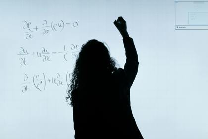 Silhouette of a person writing maths formulae on a whiteboard