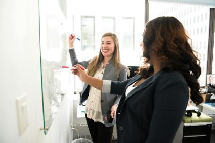 Two people in an office environment work at a whiteboard, smiling