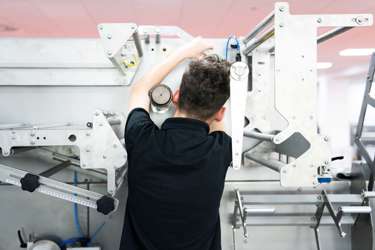 A young person works with their back to the camera operating a complex piece of machinery 