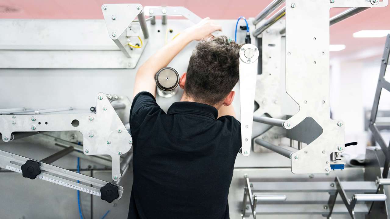 A young person works with their back to the camera operating a complex piece of machinery 