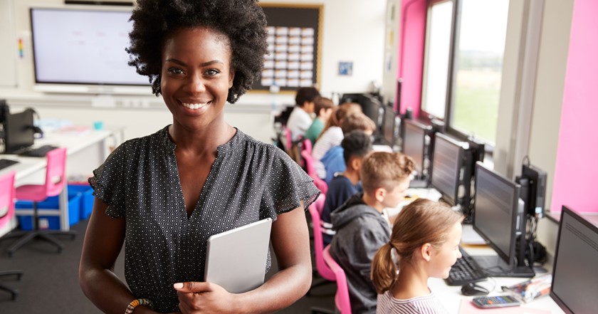 Black female computer science teacher in front of class of children using desktop computers