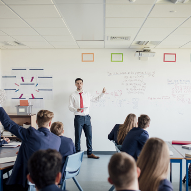 A teacher at the front of a class or secondary school students teaching. One student has their hand up