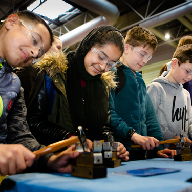 A group of young people in goggles working with hammers at a work bench