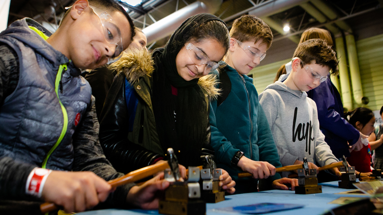 A group of young people in goggles working with hammers at a work bench