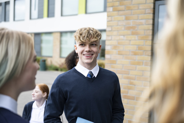 A group of young people smiling outside their school building 