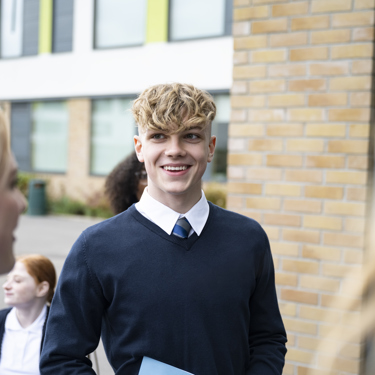 A group of young people smiling outside their school building 