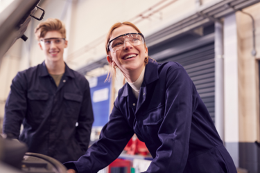 Two young people in overalls and goggles smile at work