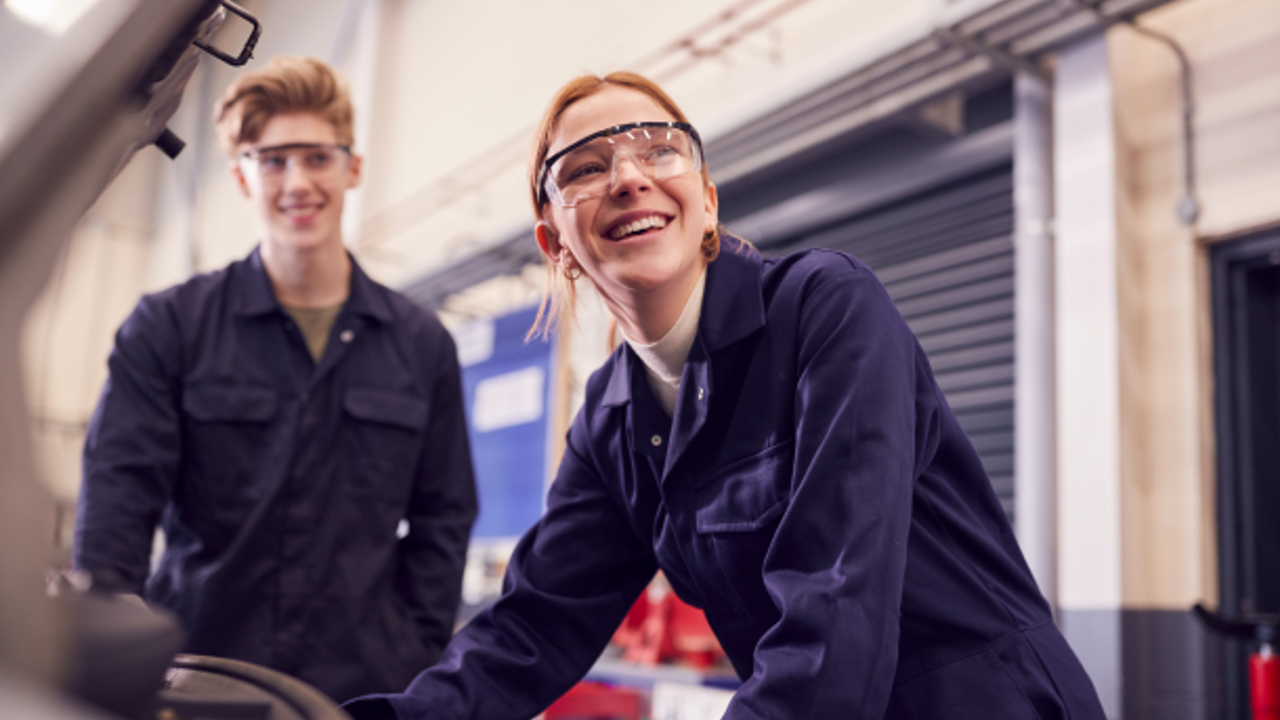 Two young people in overalls and goggles smile at work