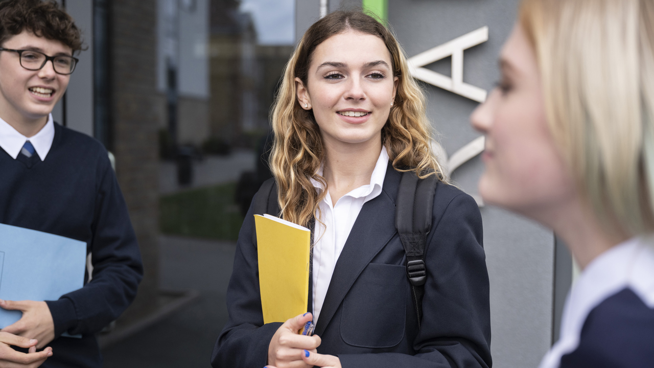 Three young people talking outside school holding folders