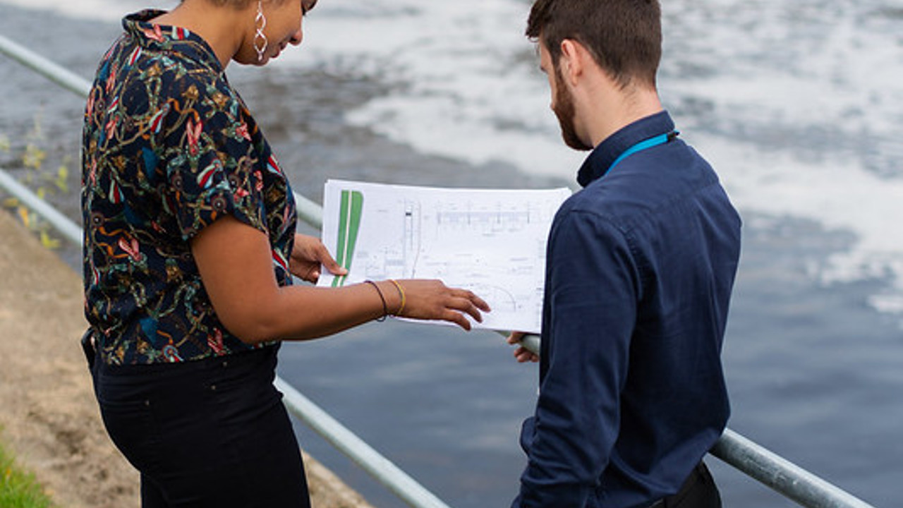 Two people stand by some water works looking at plans