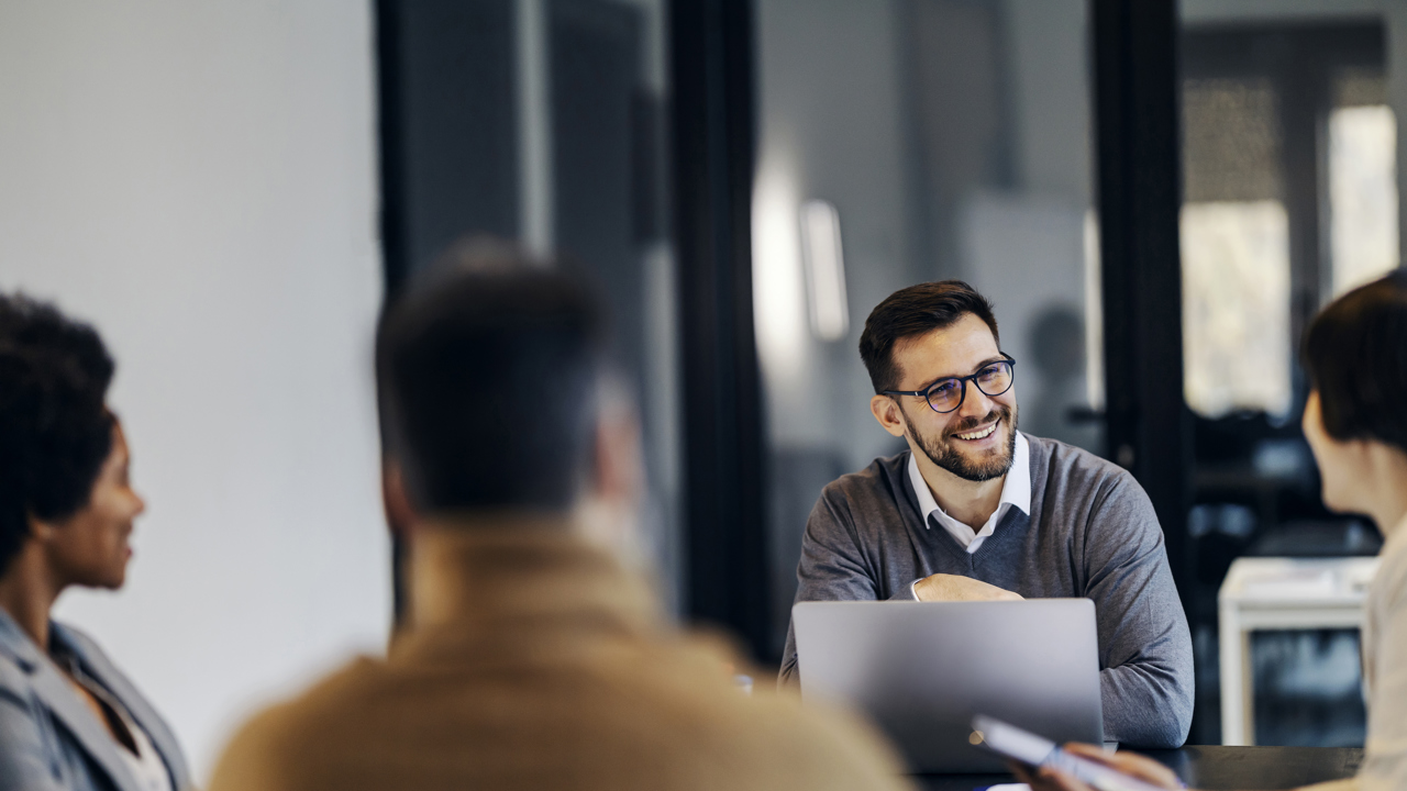 A group of people at work sit around a meeting table talking 