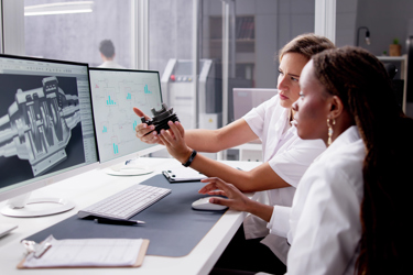 Two engineers sit at a desk looking at screens and equipment