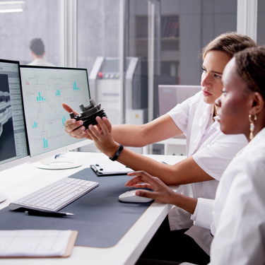 Two engineers sit at a desk looking at screens and equipment