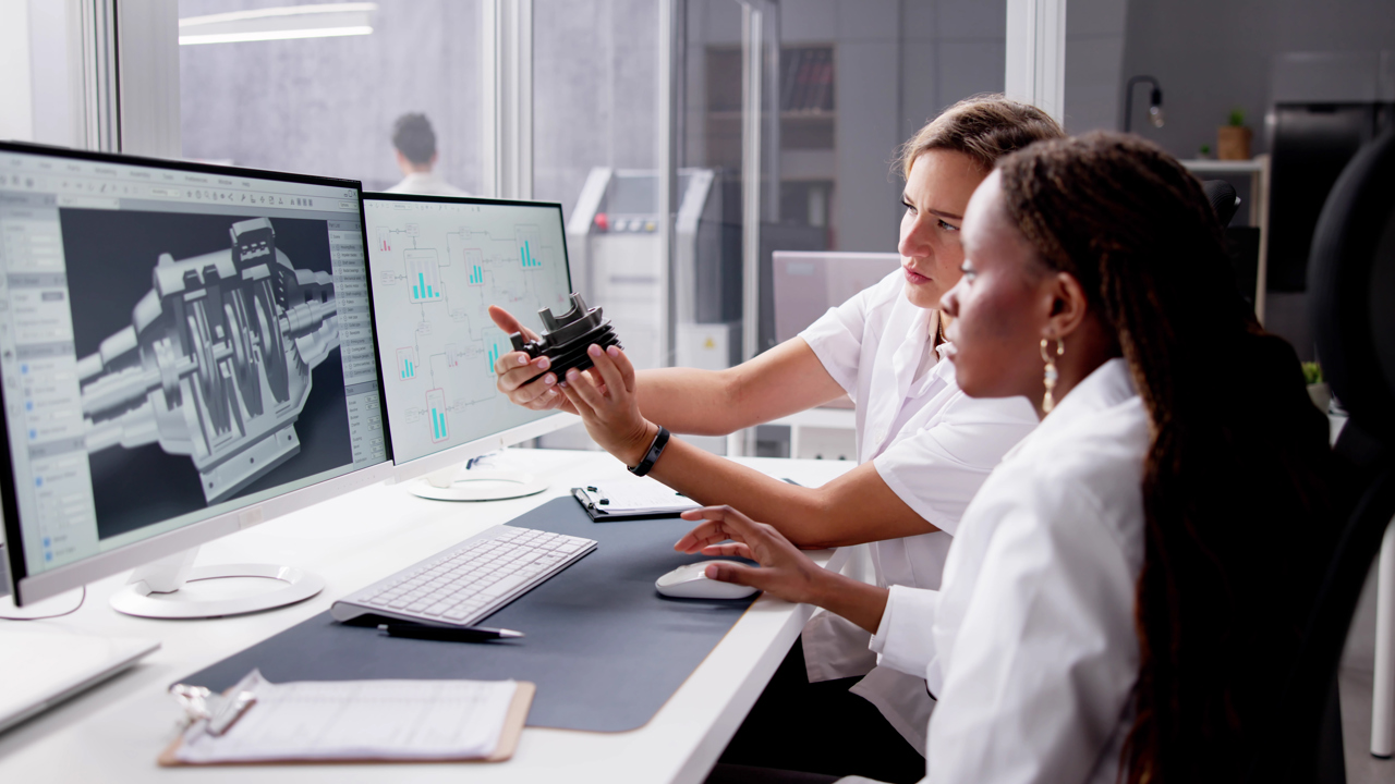 Two engineers sit at a desk looking at screens and equipment