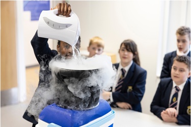 Young people in school science lab working on an experiment as others look on 