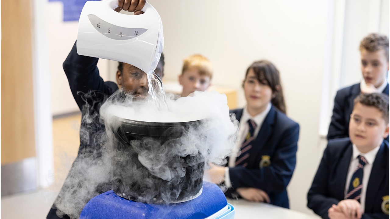 Young people in school science lab working on an experiment as others look on 