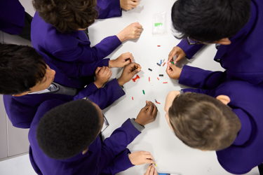 A group of young people around a table shot from above, they're using materials on the desk