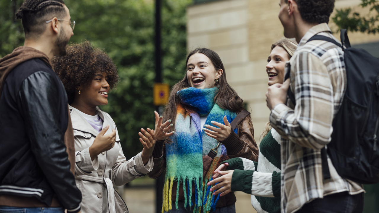 A group of young adults talk animatedly in a group outside