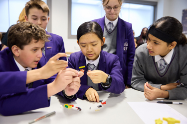 A group of young people around a table, they're using materials on the desk to build