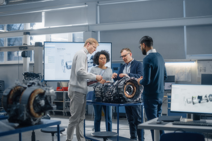 Four engineers stand in a workshop around a large piece of equipment