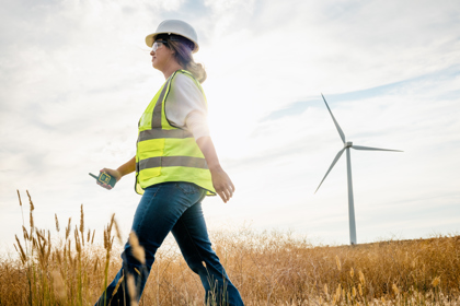 Engineer in hard hat and high vis walks past a wind turbine 