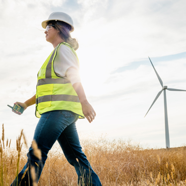 Engineer in hard hat and high vis walks past a wind turbine 