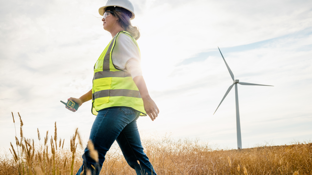 Engineer in hard hat and high vis walks past a wind turbine 