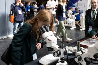 A young person at The Big Bang Fair looks into a microscope as others in the background walk by