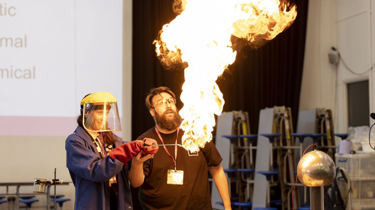 Science demonstration featuring a huge bunsen burner and flame with everyone in safety gloves and goggles