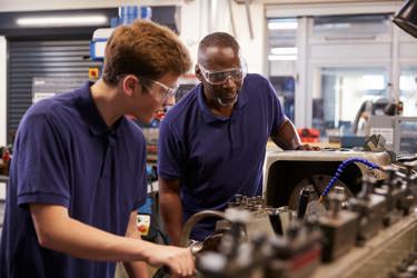 Two engineers in a workshop operating machinery they are wearing protective clothing