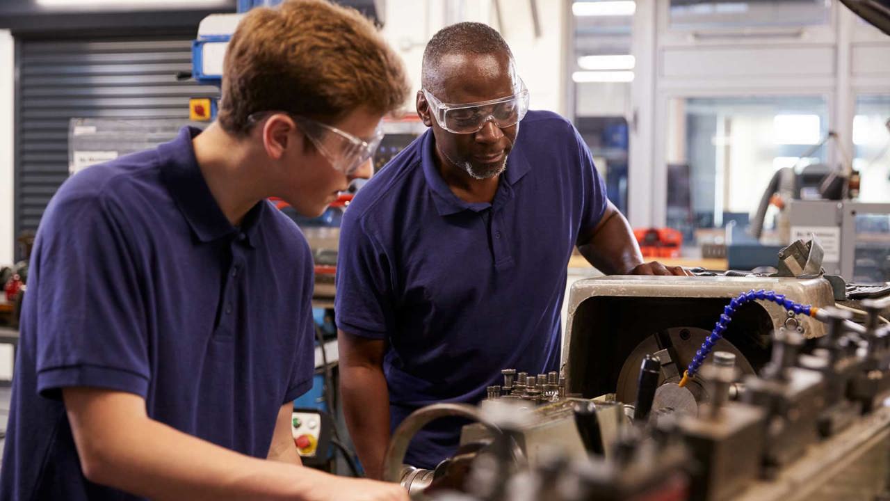 Two engineers in a workshop operating machinery they are wearing protective clothing