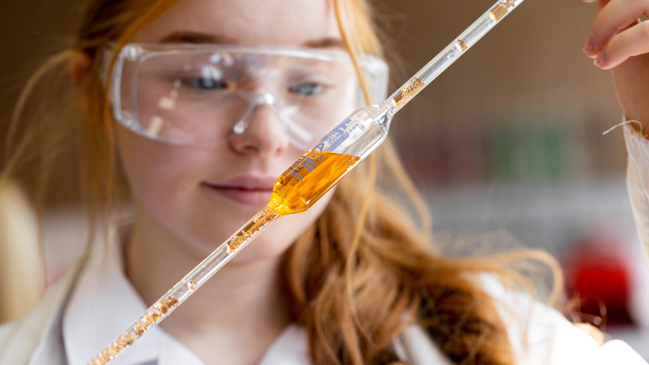 School student working on a science experiment holding up a tube of liquid