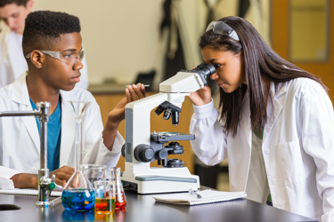 Two students working in a science lab at school working with microscopes