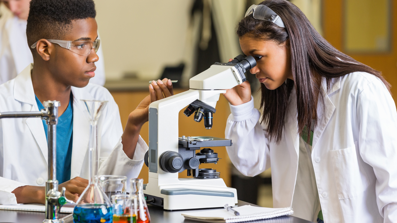 Two students working in a science lab at school working with microscopes