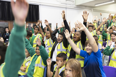 A picture of students sitting as an audience with their hands up looking excited