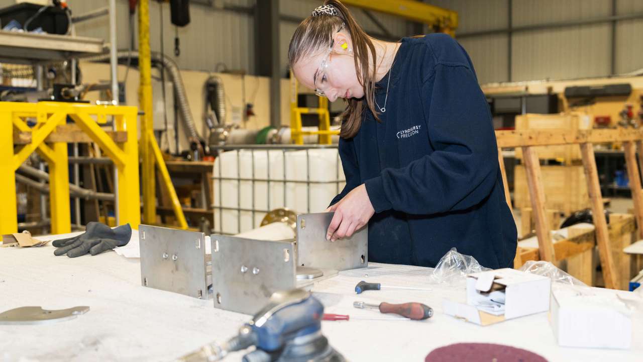 A T Level student wearing protective goggles at a work bench in a warehouse, constructing using metal pieces