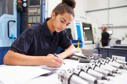 An engineer at their desk working with tools all around them. They are writing and concentrating