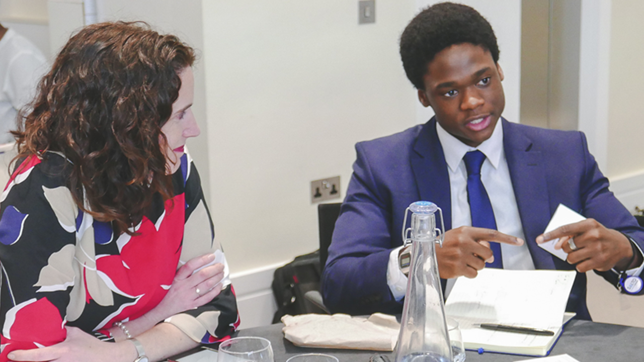 A professional and a student sit at a table discussing 