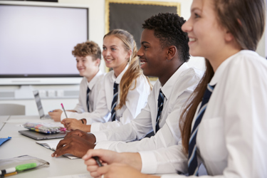 Four secondary school students in their classroom at their desks smiling