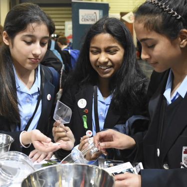 Three young people interact with exhibits and stands and activities at The Big Bang Fair