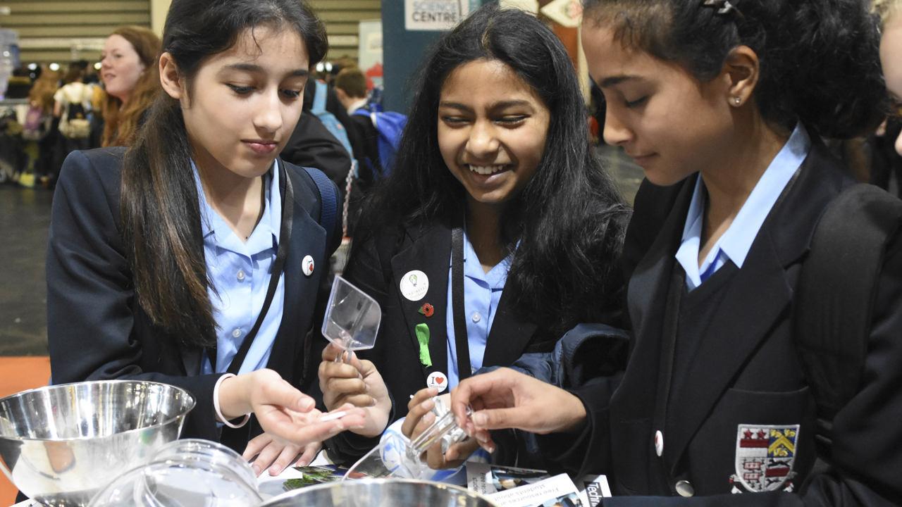 Three young people interact with exhibits and stands and activities at The Big Bang Fair