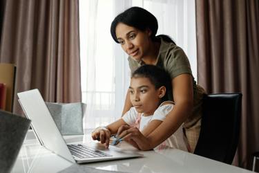 Primary aged pupil working on a laptop with the help of an adult