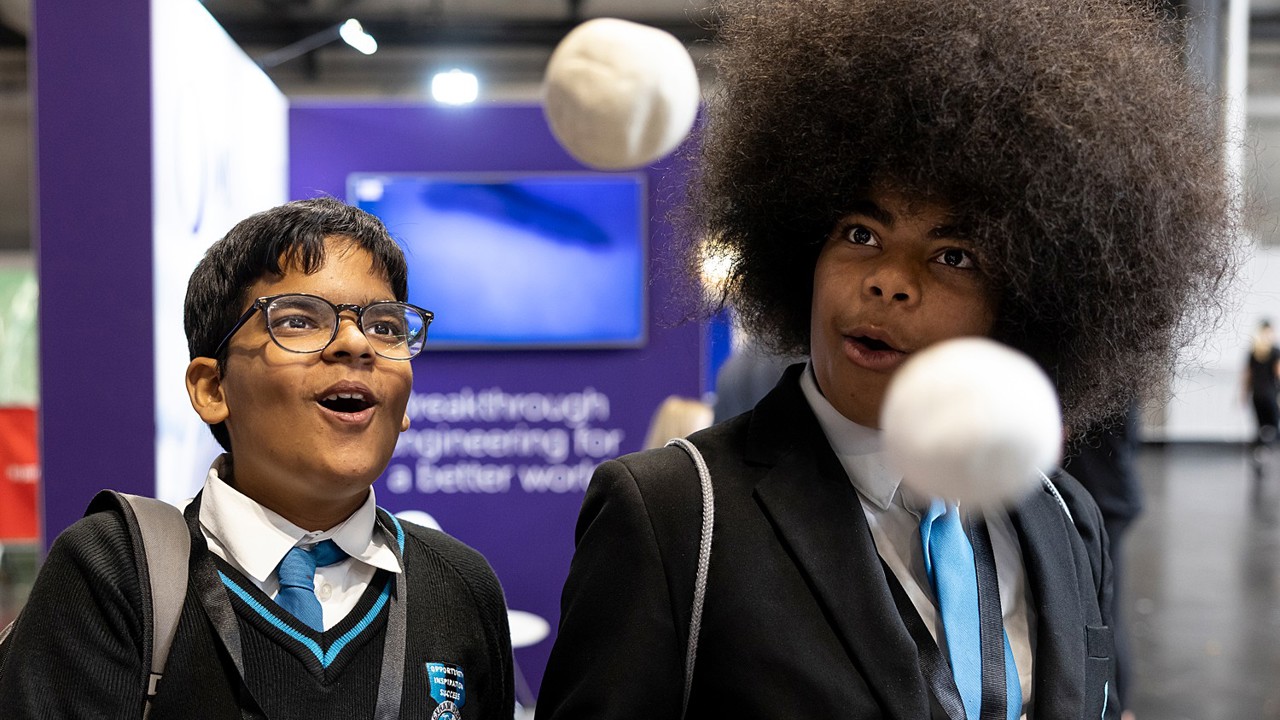 Two young people with expressive faces marvel at a scientific experiment at The Big Bang Fair. In front of them two balls seem to float mid air.