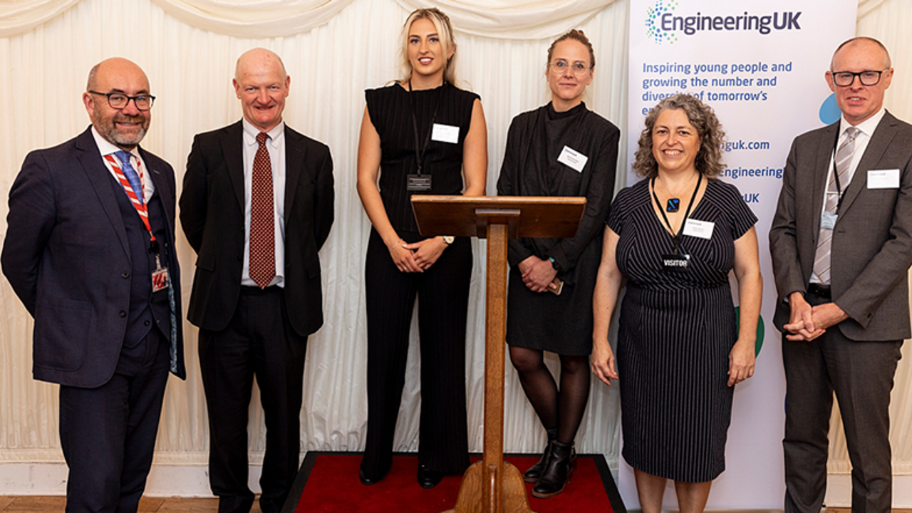 A group of professionals stand on a stage with a lectern facing the camera smiling 