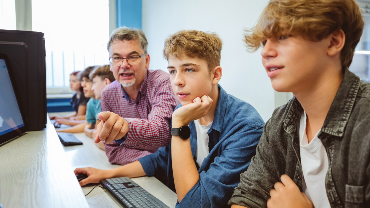 A group of students and their teacher in a school computer lab looking at screens