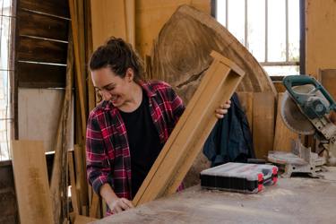 Someone in a workshop holding a piece of wood with equipment and toolbox around them