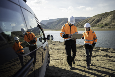 Two engineers in high vis and hard hats outside with a laptop as they walk towards a vehicle 