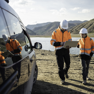 Two engineers in high vis and hard hats outside with a laptop as they walk towards a vehicle 