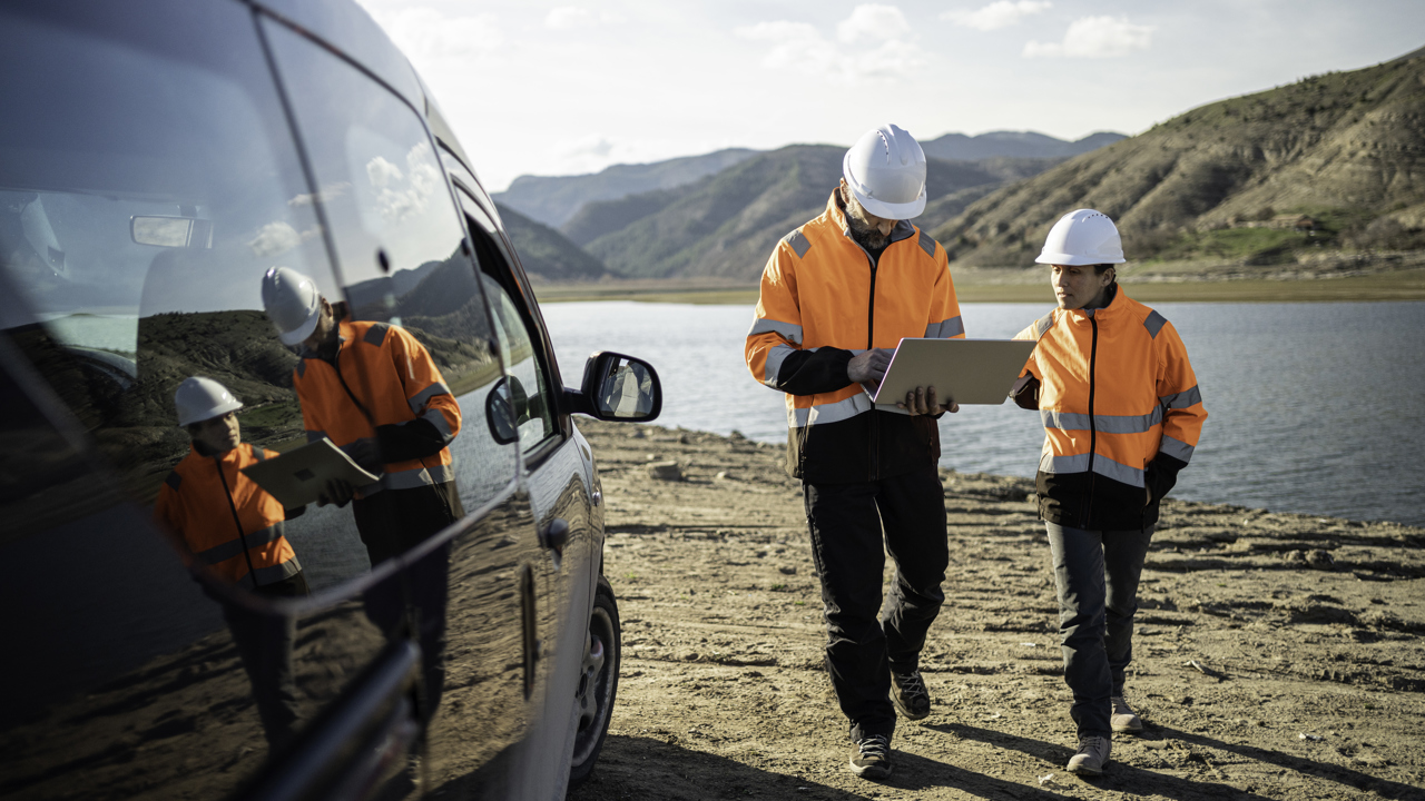 Two engineers in high vis and hard hats outside with a laptop as they walk towards a vehicle 